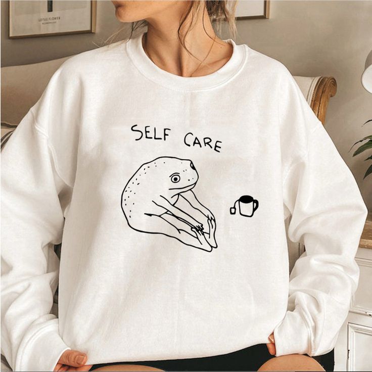 Funny white sweatshirt with a stretching frog cartoon and the text “Self Care” above it.