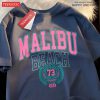 Navy unisex t-shirt featuring Malibu Beach retro-style print in varsity font with pink and teal colors.