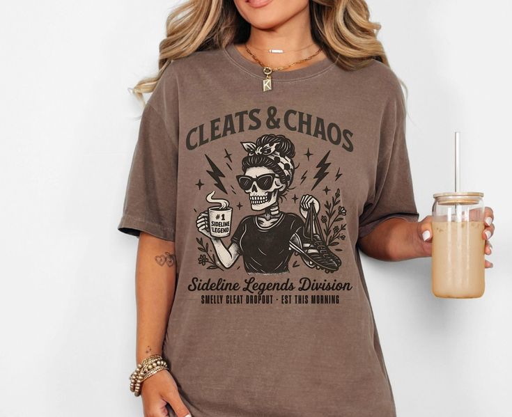 Brown t-shirt with “Cleats & Chaos” skeleton mom graphic holding coffee mug and cleats, with lightning bolt accents.