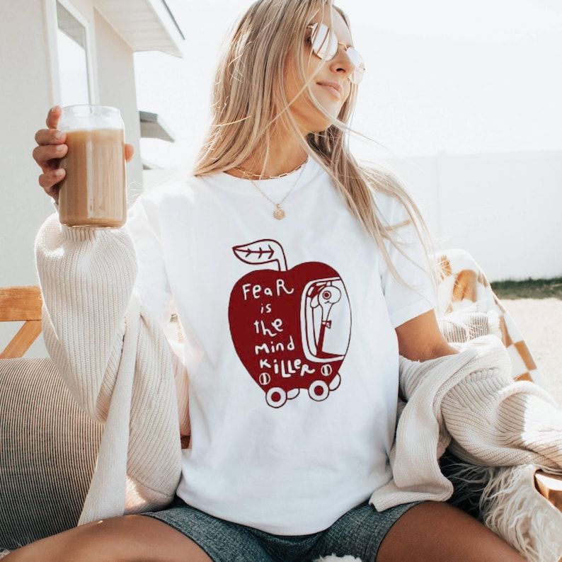 Woman wearing white Wormy Dune “Fear Is the Mind Killer” t-shirt with red apple and worm illustration.