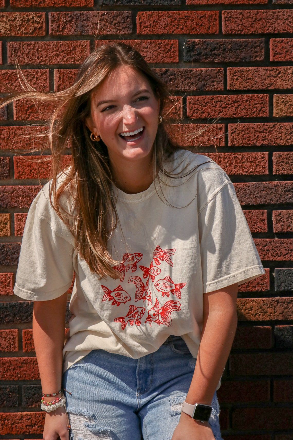 Beige t-shirt featuring a group of hand-drawn red goldfish in a minimalist, sketch-style design