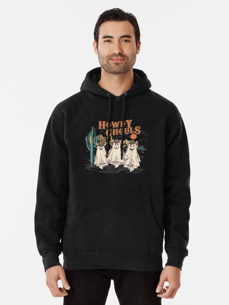 Howdy Ghouls Spooky Season Cowgirl Halloween Hoodie Black Hoodie featuring three cartoon ghost cowgirls in a desert scene with “Howdy Ghouls” text, worn by male model
