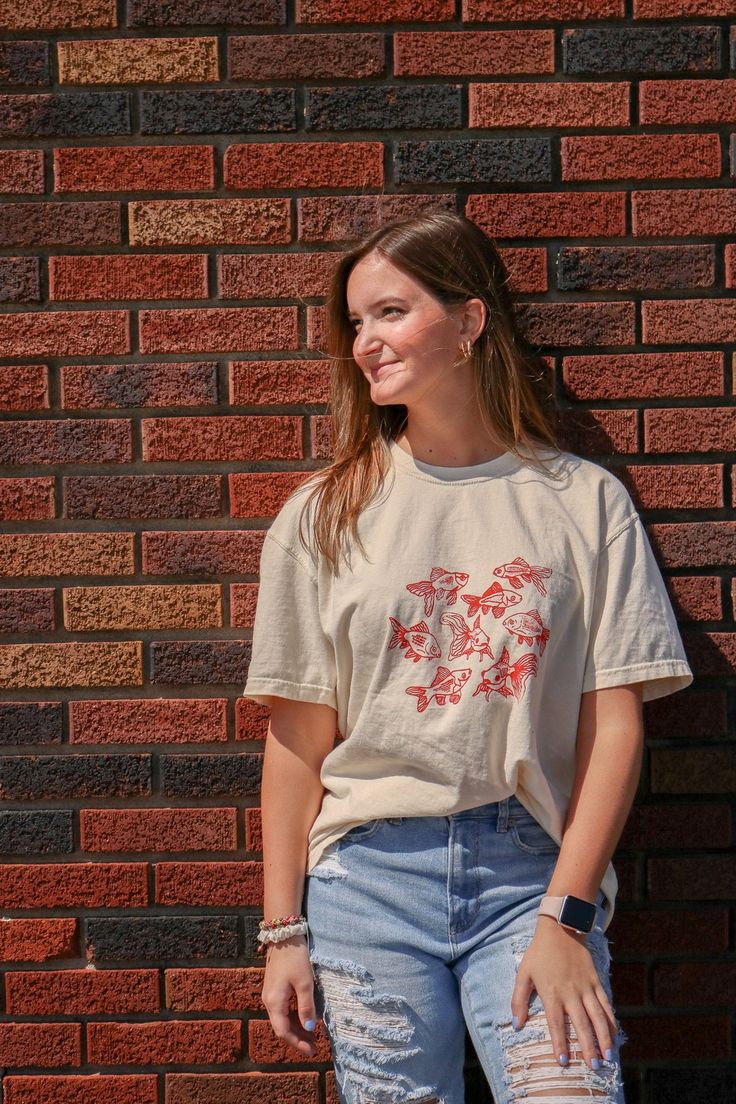 Beige t-shirt featuring a group of hand-drawn red goldfish in a minimalist, sketch-style design
