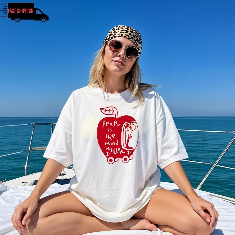 Woman wearing white Wormy Dune “Fear Is the Mind Killer” t-shirt with red apple and worm illustration.