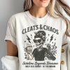 White t-shirt with “Cleats & Chaos” skeleton mom graphic holding coffee mug and cleats, with lightning bolt accents.