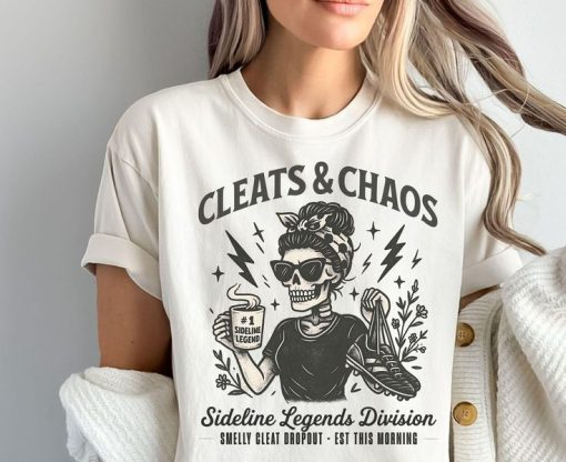 White t-shirt with “Cleats & Chaos” skeleton mom graphic holding coffee mug and cleats, with lightning bolt accents.