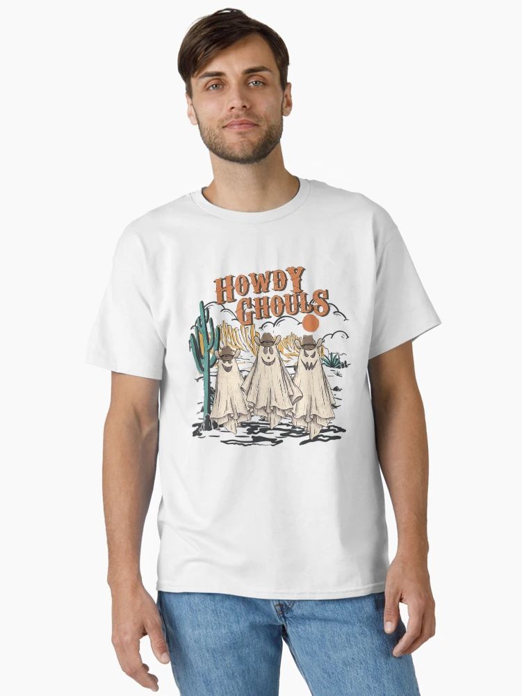 Howdy Ghouls Spooky Season Cowgirl Halloween Tee White t-shirt featuring three cartoon ghost cowgirls in a desert scene with “Howdy Ghouls” text, worn by male model
