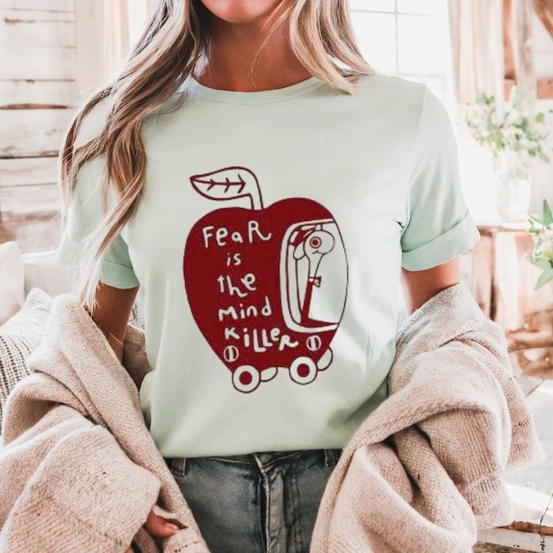 Woman wearing white Wormy Dune “Fear Is the Mind Killer” t-shirt with red apple and worm illustration.